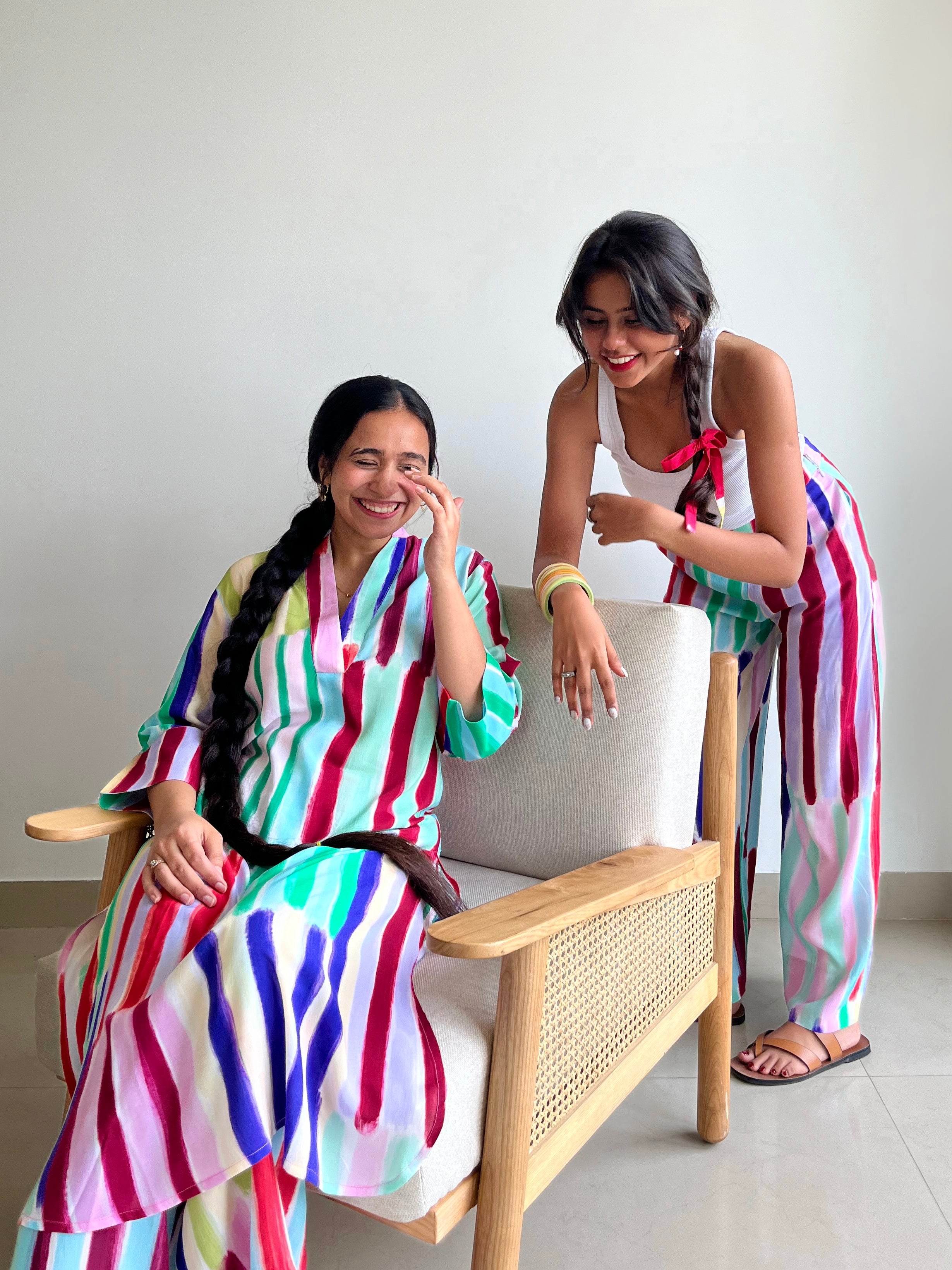 Two women wearing Imsoo circular fashion outfits sitting on a chair indoors.