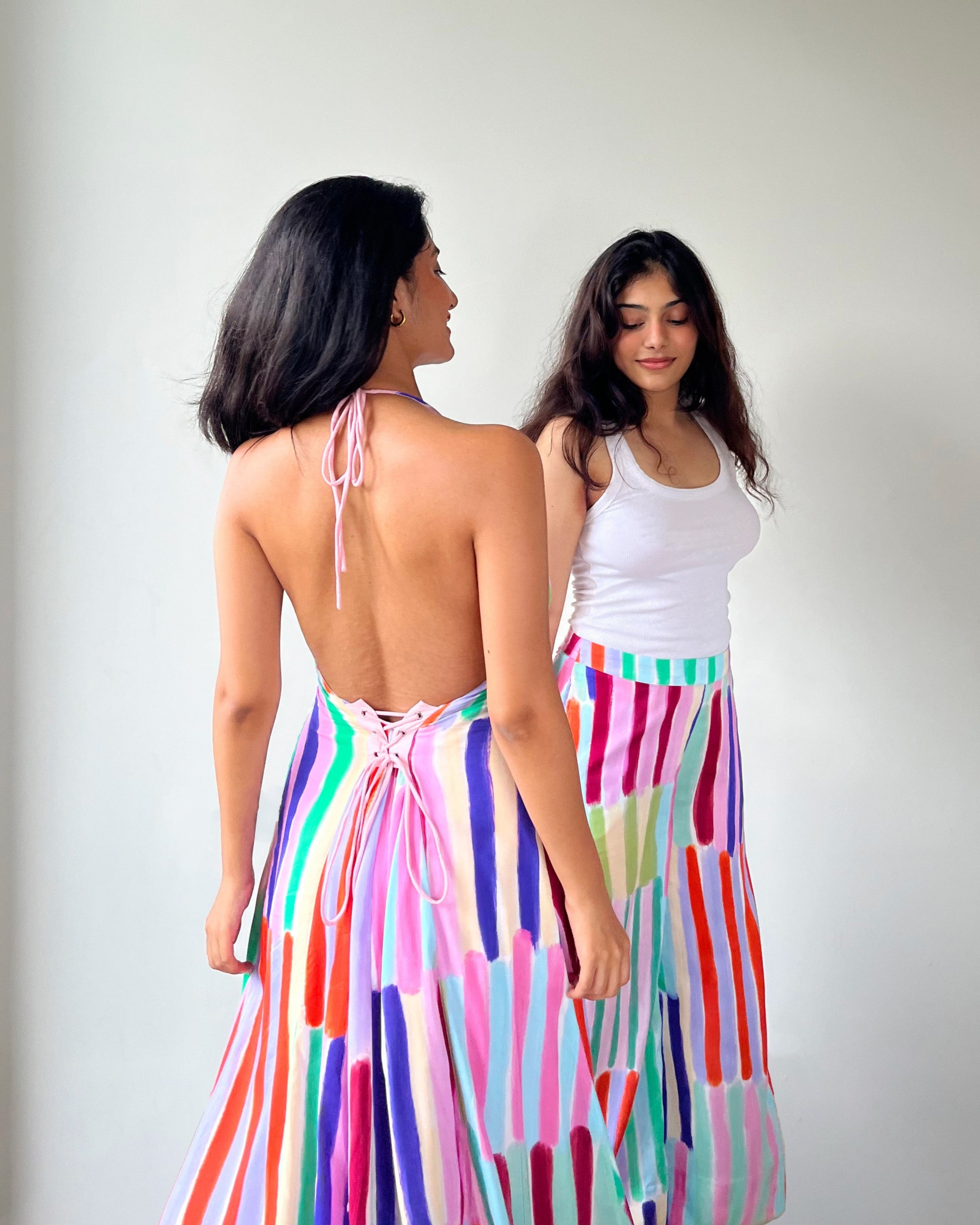 Two women standing back-to-back wearing colorful and patterned dresses against a plain background.