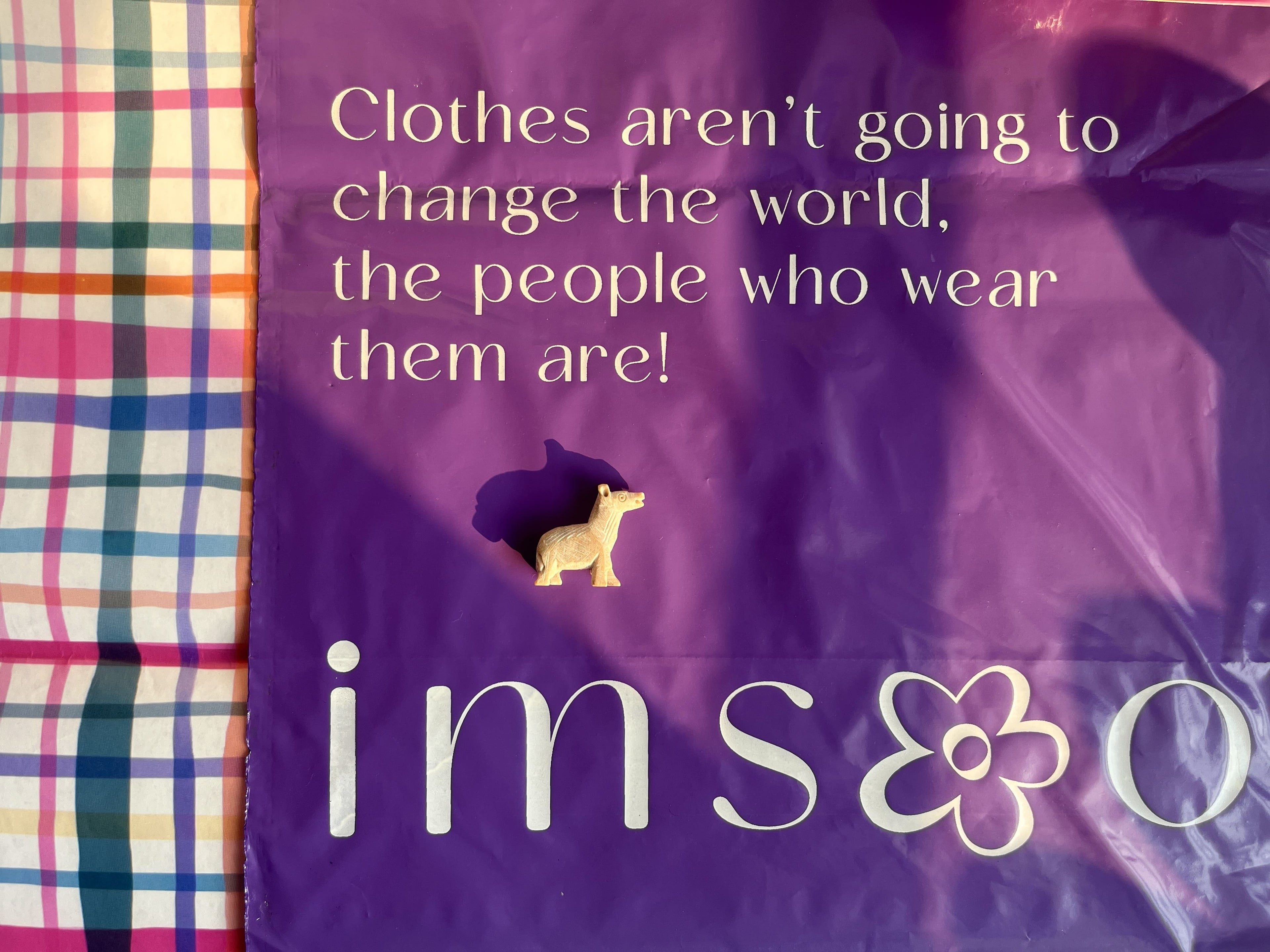Purple bag with quote and a small yellow figure on a plaid fabric background