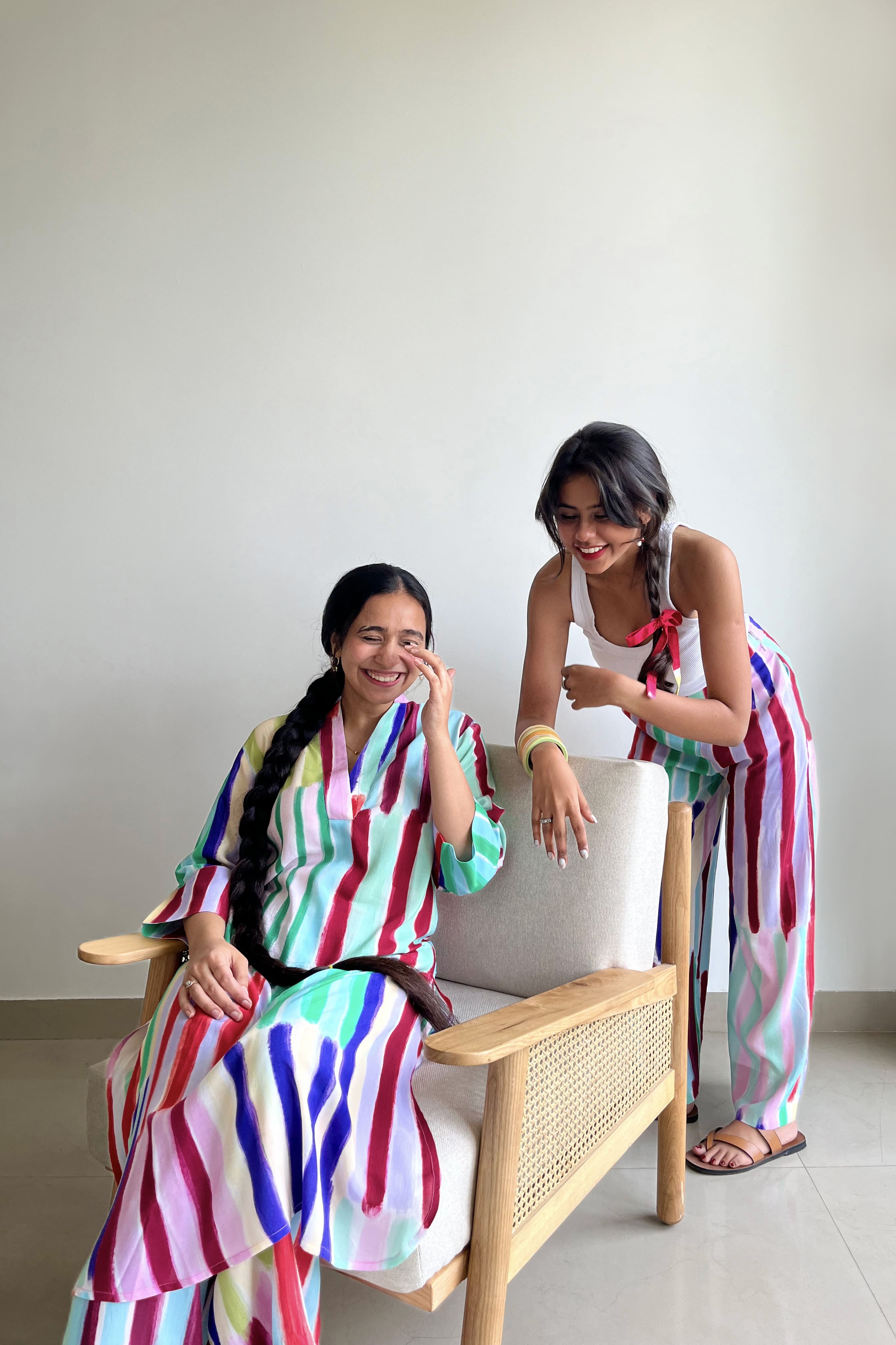 Two women wearing Imsoo circular fashion outfits sitting on a chair indoors.