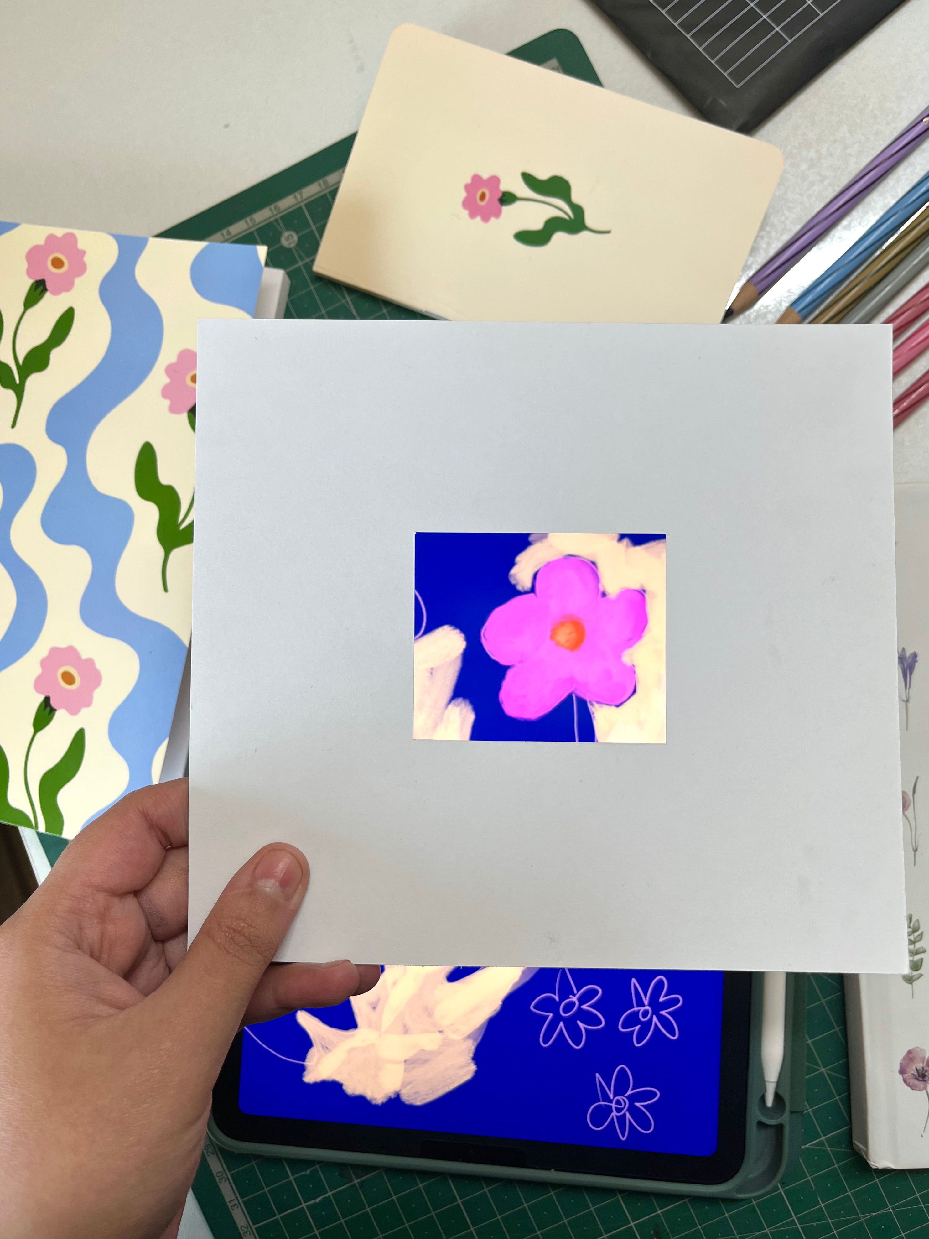 Hand holding a white card with a flower design over a digital screen displaying a floral pattern.